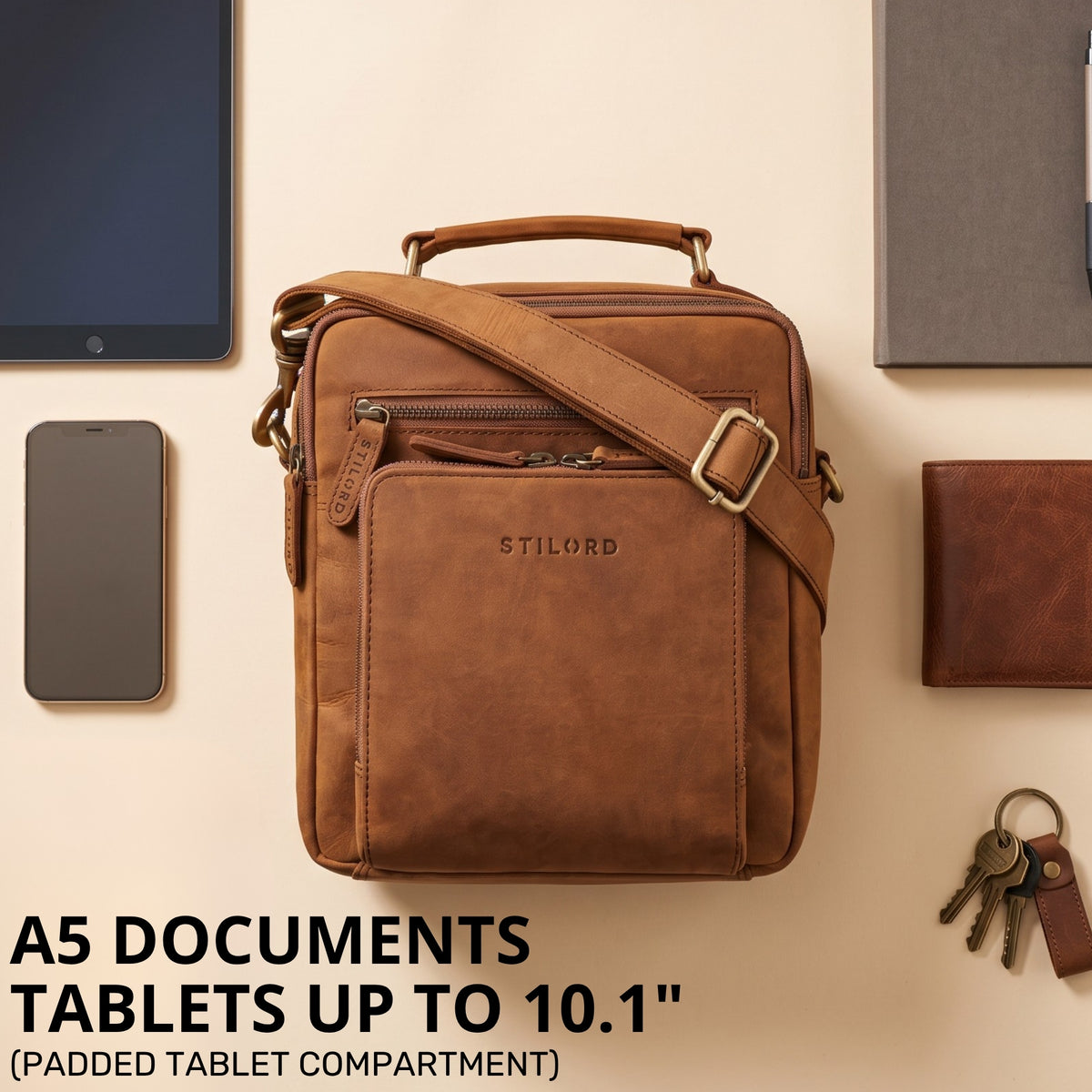 Small leather crossbody bag in tan with top handle and shoulder strap, front view with STILORD embossing, shown with tablet and keys